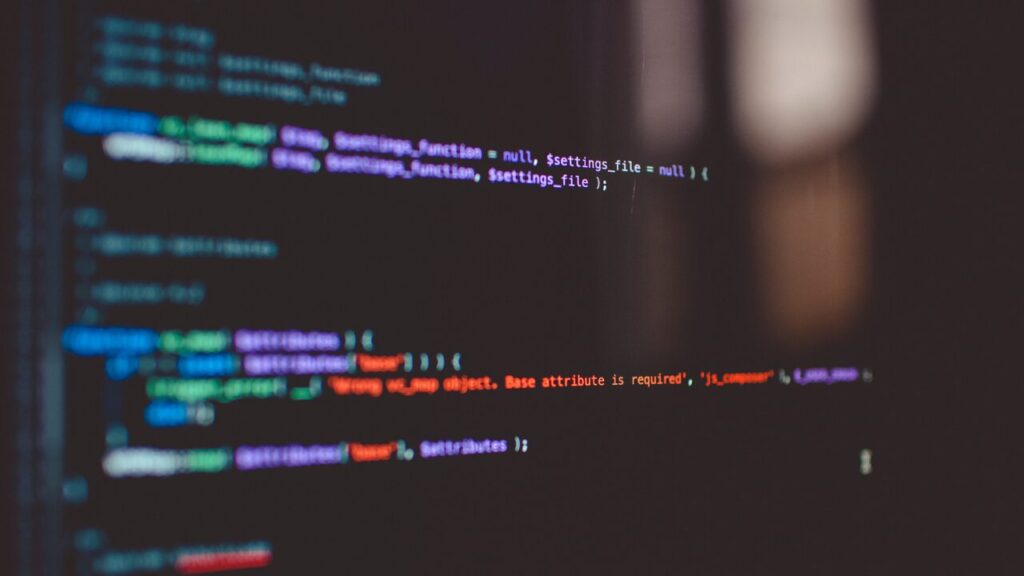 Tela de computador com fundo escuro exibindo linhas de código de programação coloridas (sintaxe destacada em azul, roxo e laranja) com efeito de desfoque (bokeh) ao fundo.